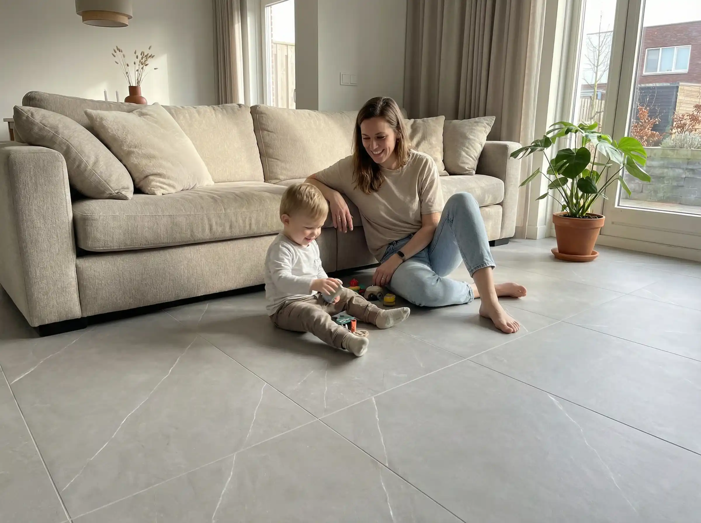 Mutter spielt mit Kind auf modernem grauen Fliesenboden im Wohnzimmer