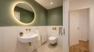 Weiße Wandfliesen und ein beleuchteter Rundspiegel vergrößern optisch den Raum beim Gäste-WC renovieren
